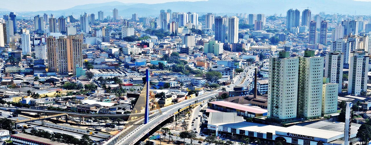 Vista elevada de Guarulhos, São Paulo, com o Viaduto Cidade de Guarulhos (ponte estaiada), prédios do centro e do bairro Macedo e a Serra da Cantareira ao fundo